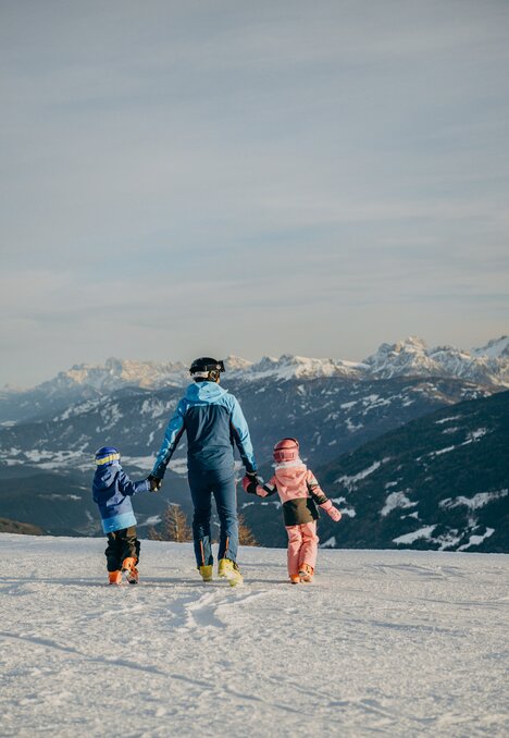 Tre persone camminano su un pendio innevato con le cime alpine sullo sfondo.