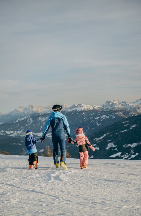 Tre persone camminano su un pendio innevato con le cime alpine sullo sfondo.