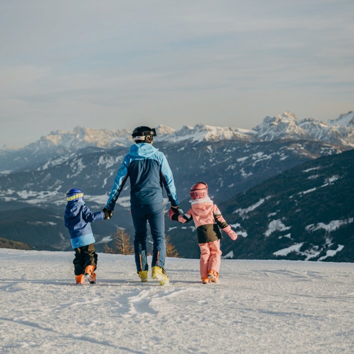 Tre persone camminano su un pendio innevato con le cime alpine sullo sfondo.