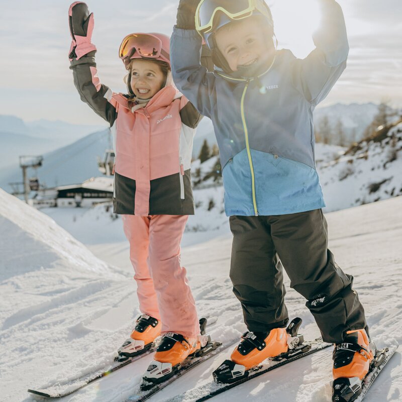 Due bambini sciano insieme su una pista innevata e soleggiata a Brixen Südtirol.