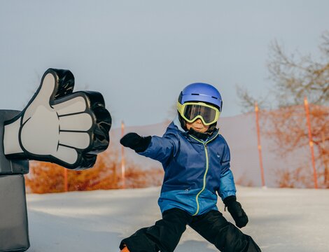 Bambino scia su una pista innevata con il pollice in su.
