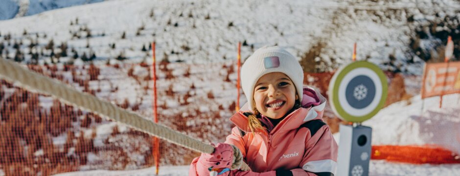 Bambina su un percorso di corde nella neve con piste da sci e montagne sullo sfondo