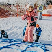 Bambina su un percorso di corde nella neve con piste da sci e montagne sullo sfondo
