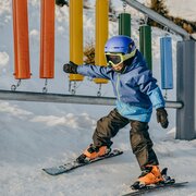 Bambino con abbigliamento invernale blu che scivola su una pista innevata in snowboard.