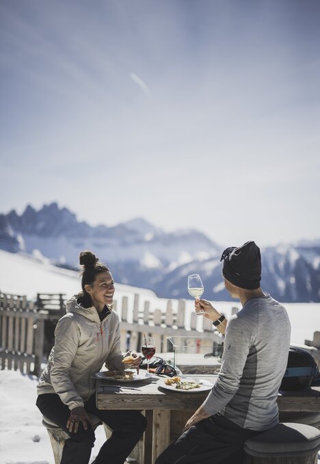 Due persone pranzano su una terrazza innevata con le Alpi sullo sfondo.
