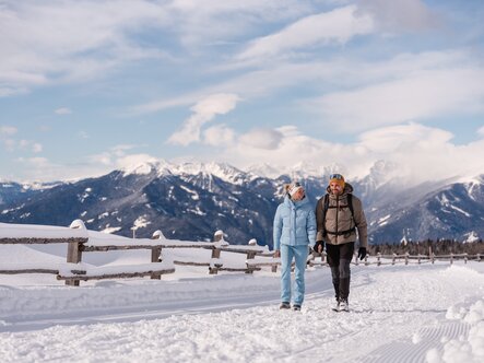Zwei Wanderer gehen auf einem verschneiten Weg mit Bergblick in Brixen Südtirol.