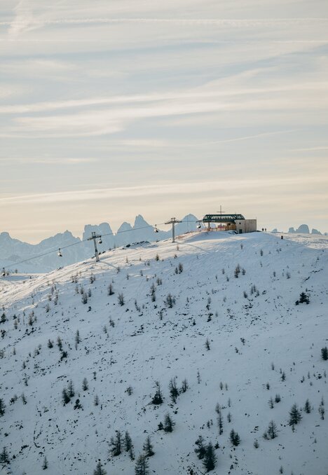 Verschneiter Skipistenhang mit Lift und Hütte in Brixen Südtirol, dahinter Berggipfel.