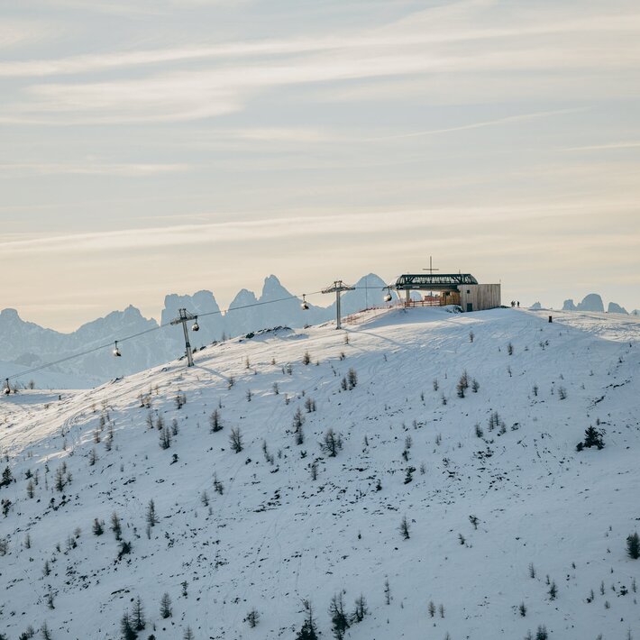 Besneeuwde skipiste met lift en berghut in Brixen Südtirol, met bergtoppen op de achtergrond.