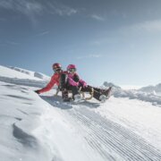 Twee mensen zitten op een besneeuwde berghelling, met heldere toppen in de verte.