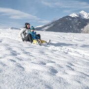 Erwachsener und Kind beim Rodeln auf einer verschneiten Hänge in Brixen Südtirol mit Alpenpanorama.