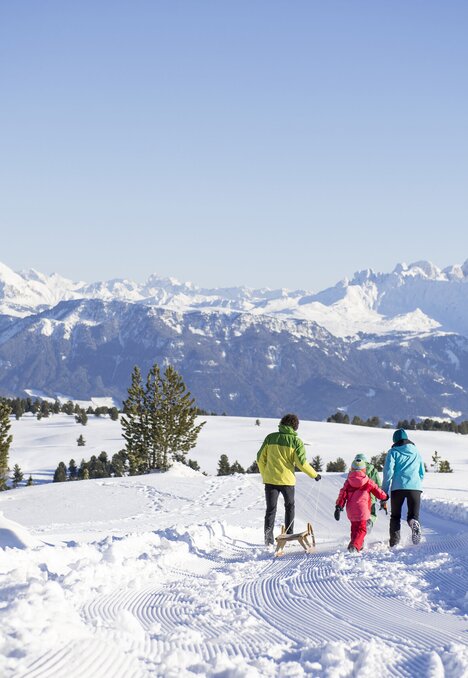 Familie wandert über eine verschneite Hochebene mit den Dolomiten im Hintergrund, Brixen Südtirol