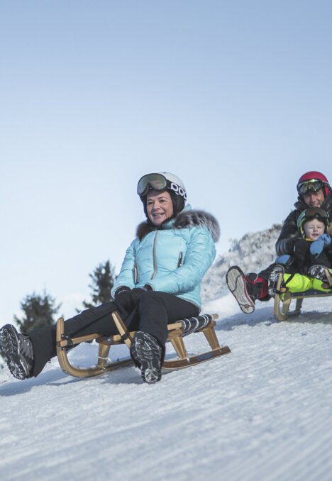 Kinder rodeln auf einer verschneiten Piste im Winter in Brixen Südtirol.