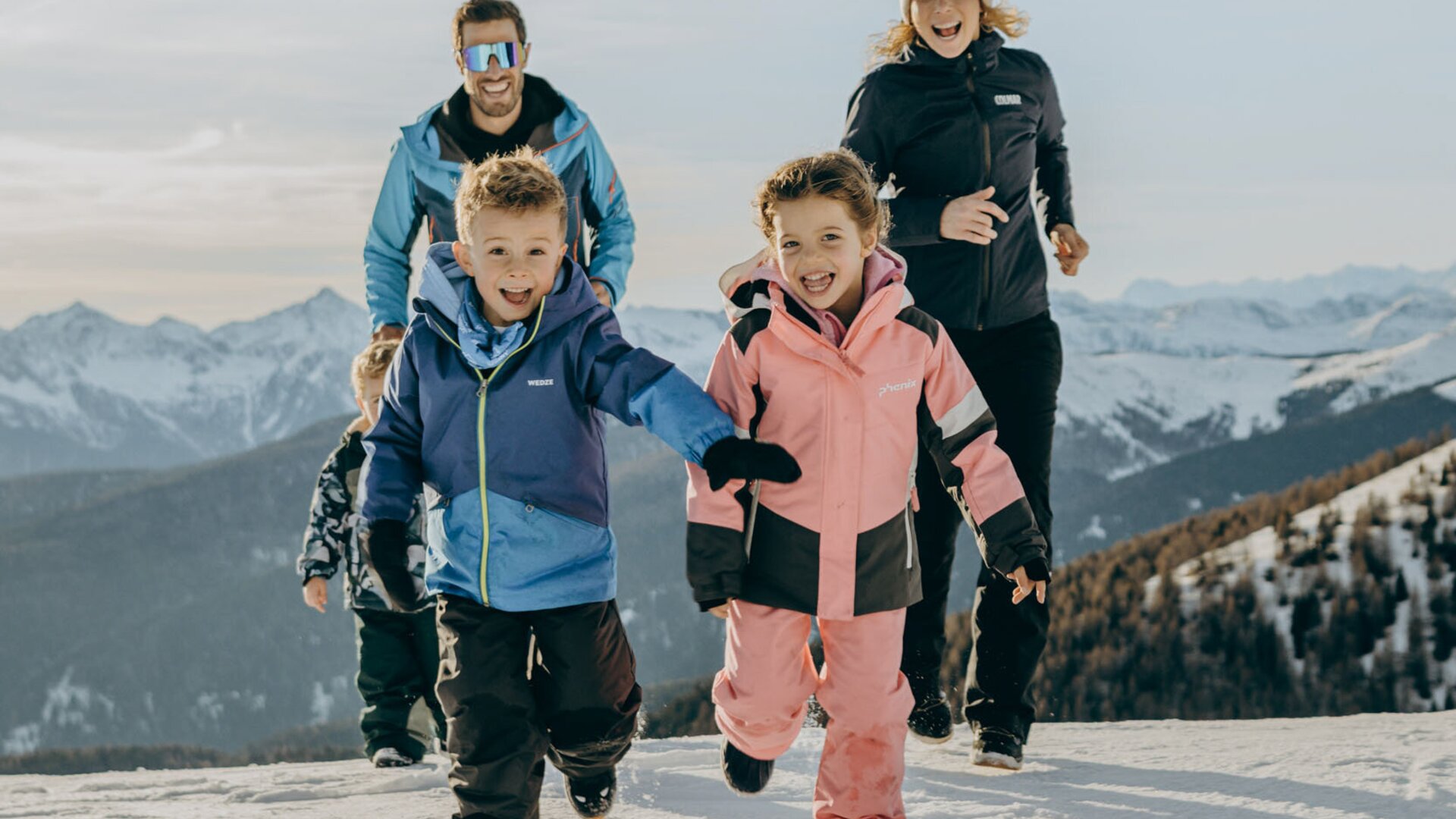 Family walking uphill through fresh snow on a mountain slope in winter.