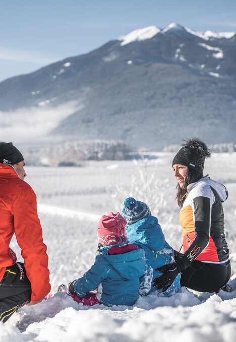 Famiglia seduta nella neve fresca con vista sulle montagne di Brixen Südtirol.