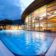 Piscina all’aperto al tramonto accanto a un moderno centro benessere con montagne sullo sfondo a Brixen Südtirol