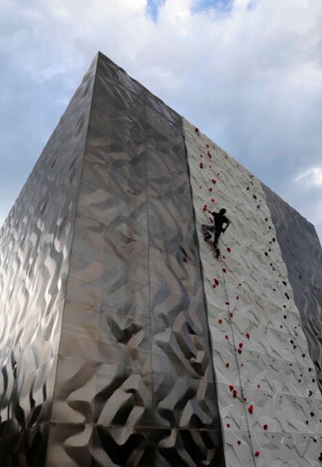 Arrampicatore su una moderna parete da arrampicata all’aperto con montagne e cielo nuvoloso sullo sfondo