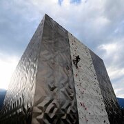 Climber on a modern outdoor climbing wall with mountain scenery and cloudy sky in the background