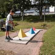 Junge spielt Minigolf neben bunten Hindernissen in einem grünen Park in Brixen Südtirol.
