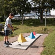 Junge spielt Minigolf neben bunten Hindernissen in einem grünen Park in Brixen Südtirol.