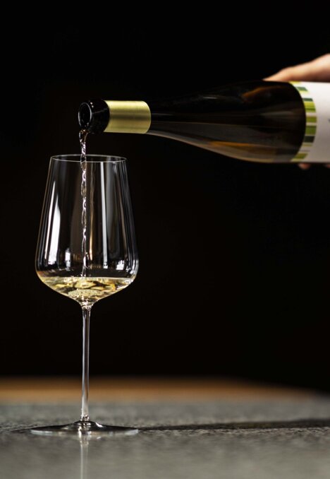 Vino bianco versato in un calice davanti a uno sfondo scuro.