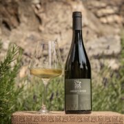 Bottiglia di vino e calice su una cassetta di legno, tra le erbe in un giardino soleggiato. | © Kainzwaldner Tobias