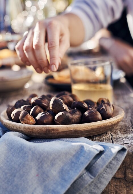 Mani che prendono castagne arrosto e uva su un tavolo rustico all'aperto.