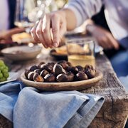 Hands reaching for roasted chestnuts and grapes at a rustic outdoor table.