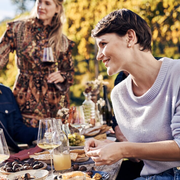 Freunde genießen Wein und regionale Speisen an einem Tisch im Freien im Herbst bei Brixen Südtirol.