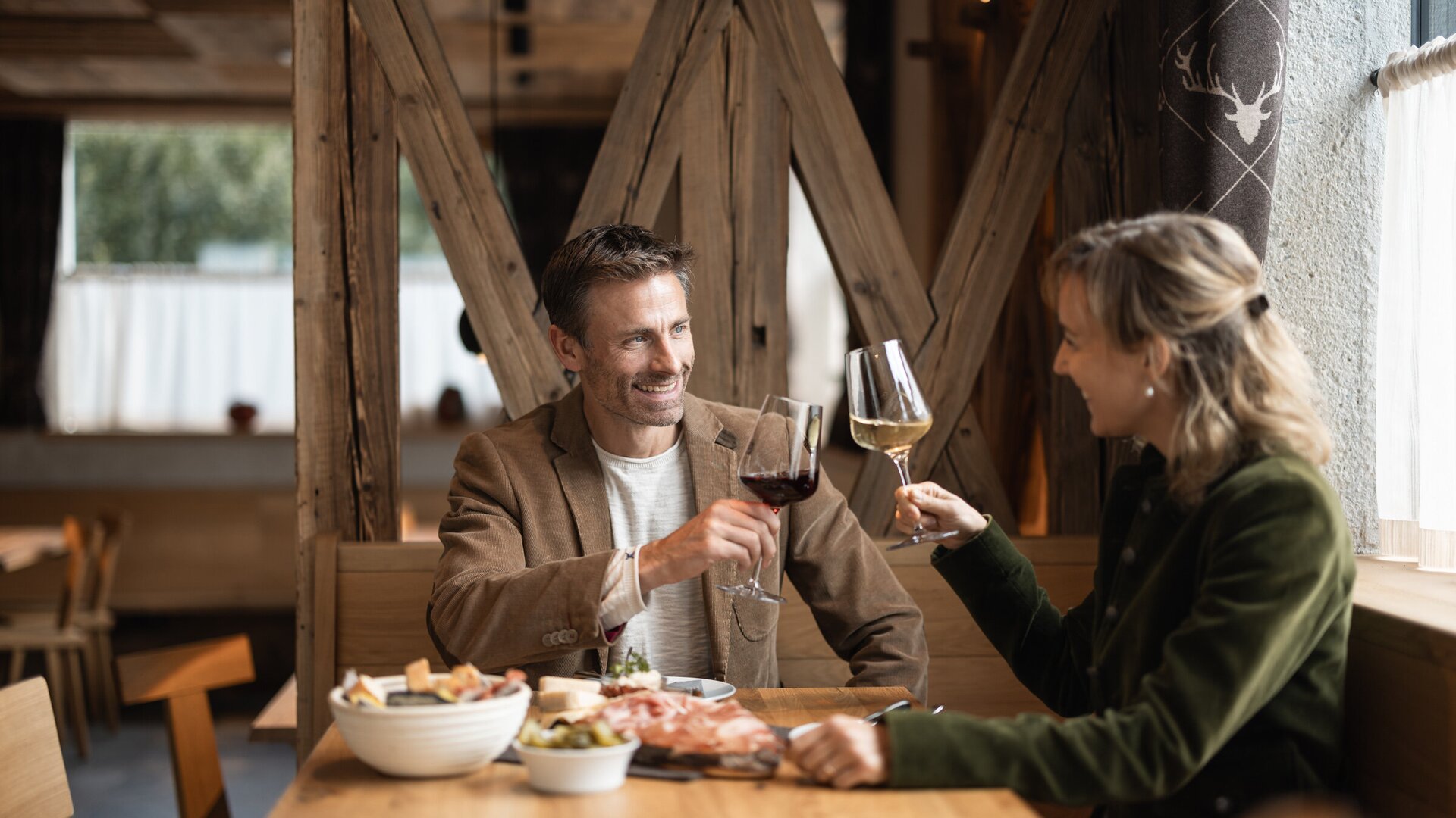 Couple toasting with red and white wine in a cozy restaurant with shared dishes on the table.