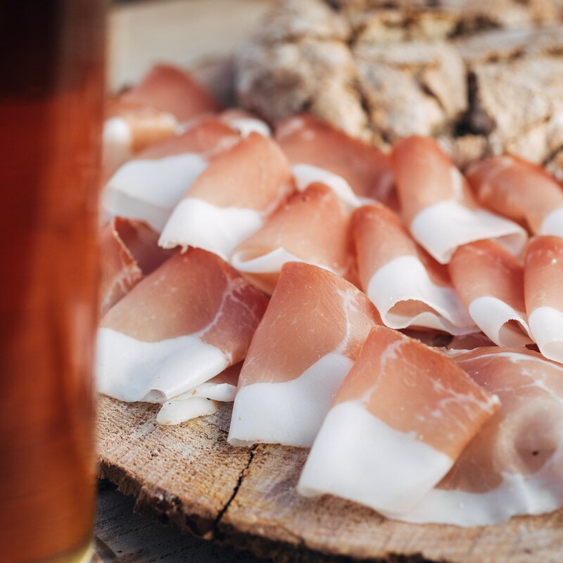 Aufgeschnittene Speck- und Schinkenstücke auf einem Holzbrett mit einem Glas Bier.