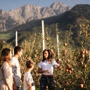 Family standing in an apple orchard with mountains in the background. | © IDM/Südtiroler Apfelkonsortium/Patrick Schwienbacher