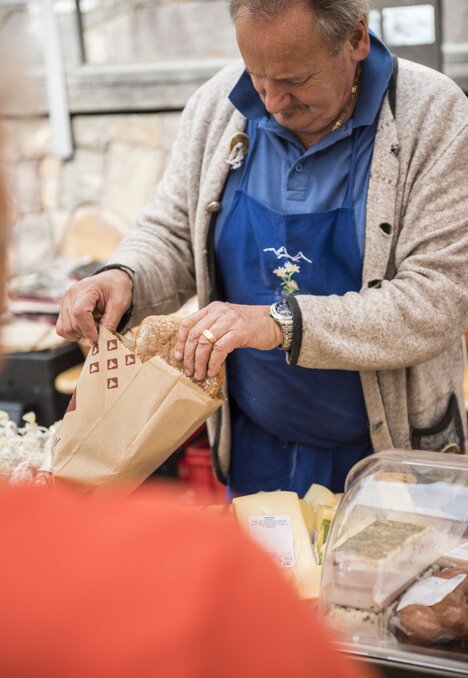 Mann packt frische Lebensmittel an einem Marktstand in eine Papiertüte.