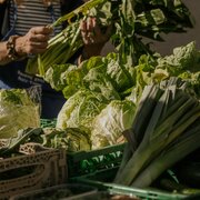 Fresh leafy vegetables at a local market, with a vendor preparing greens.