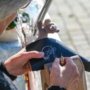 A craftsperson engraves a black leather piece by hand outdoors.
