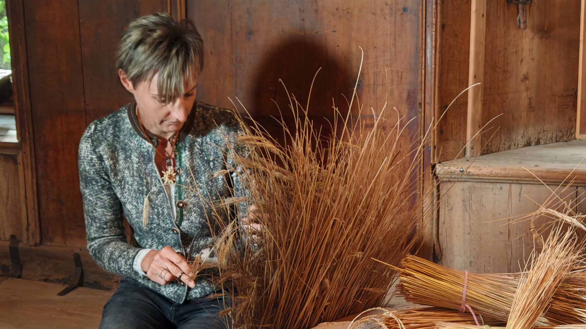 Woman crafting straw decorations in a rustic wooden room in Brixen Südtirol.