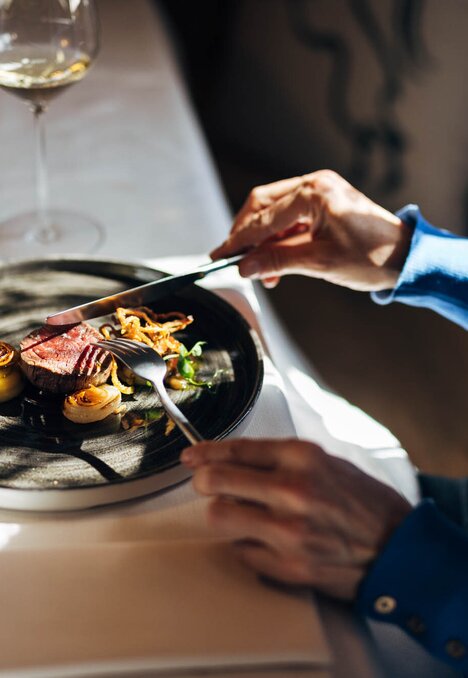 Gast genießt ein angerichtetes Restaurantgericht mit Weingläsern am Tisch