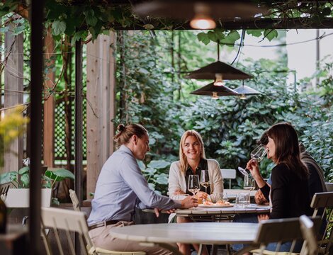 Drei Personen essen und trinken auf einer grünen Terrasse im Freien.