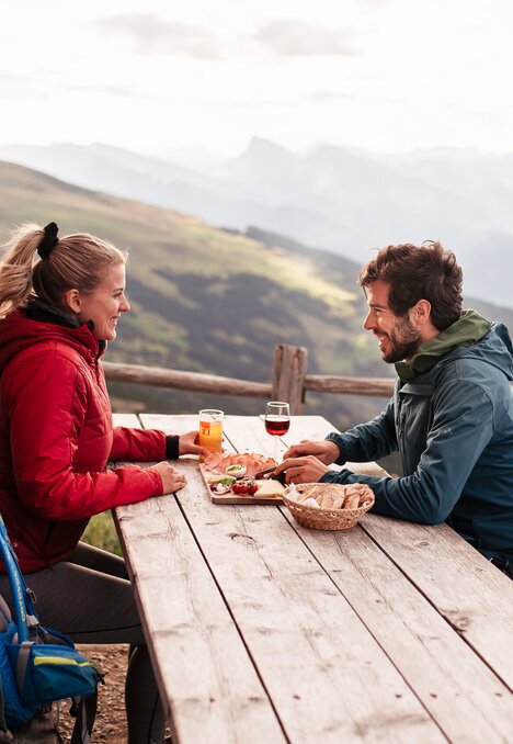 Coppia che mangia e beve in una malga di montagna con vista panoramica sulle Alpi.