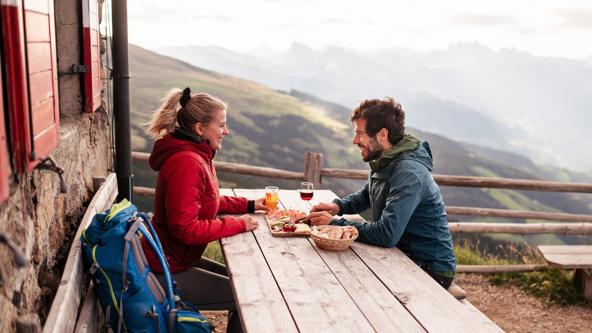 Couple enjoying a meal and drinks at a mountain hut with panoramic alpine views.