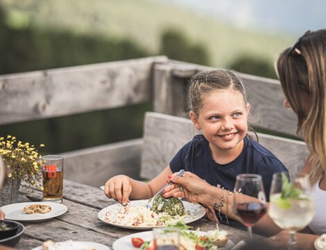 Familie speist auf einer Holzterrasse in Brixen Südtirol mit Bergpanorama im Hintergrund.