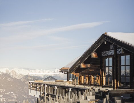 Terras van een bergrestaurant met besneeuwde Alpenpieken onder een heldere lucht.