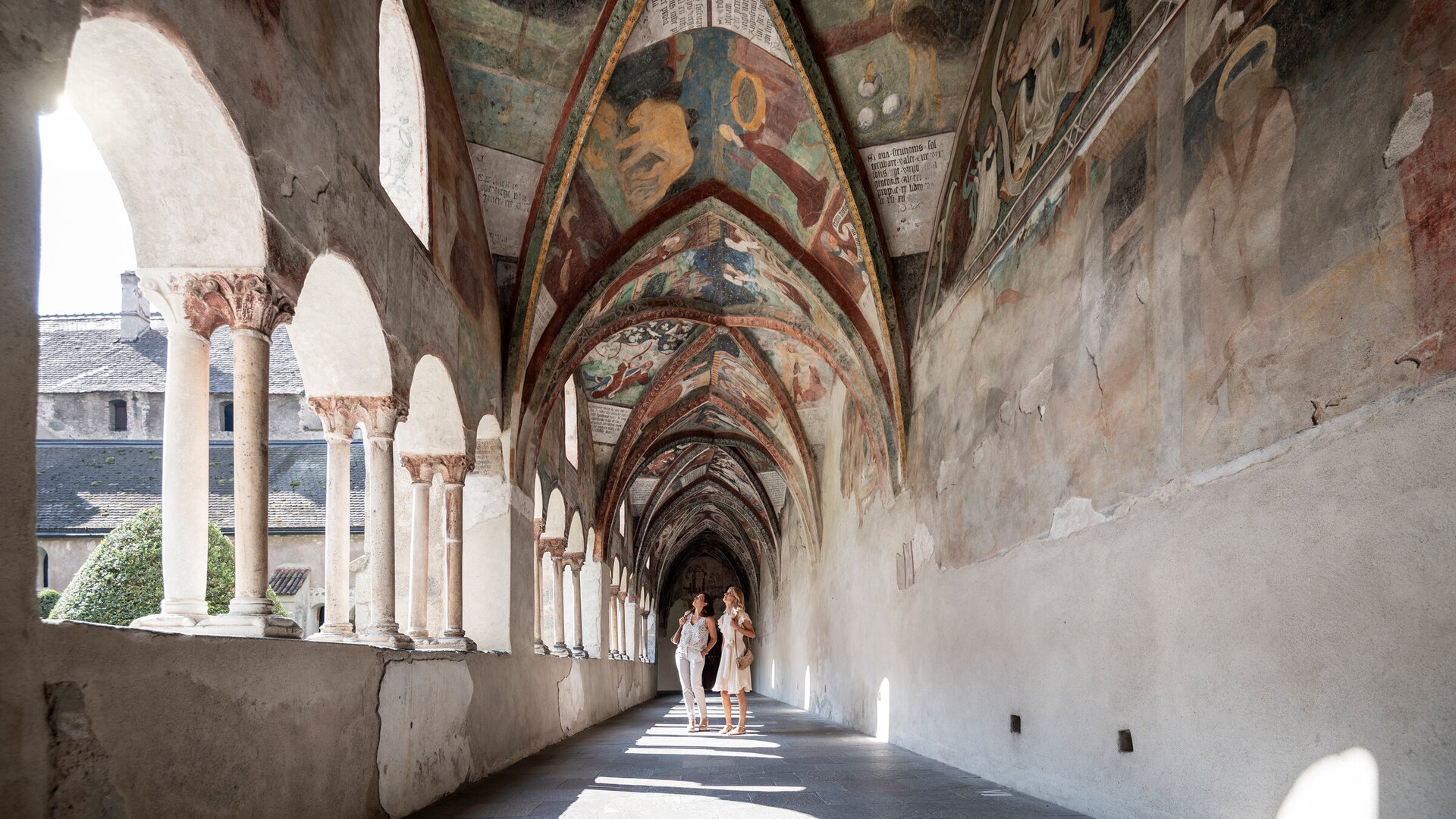 Frescoed cloister corridor with arches in Brixen Südtirol, with two people walking | © IDM Südtirol-Alto Adige/Alex Filz