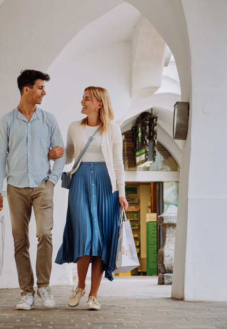 Coppia che passeggia sotto un passaggio ad archi bianco a Brixen Südtirol con borse per lo shopping.