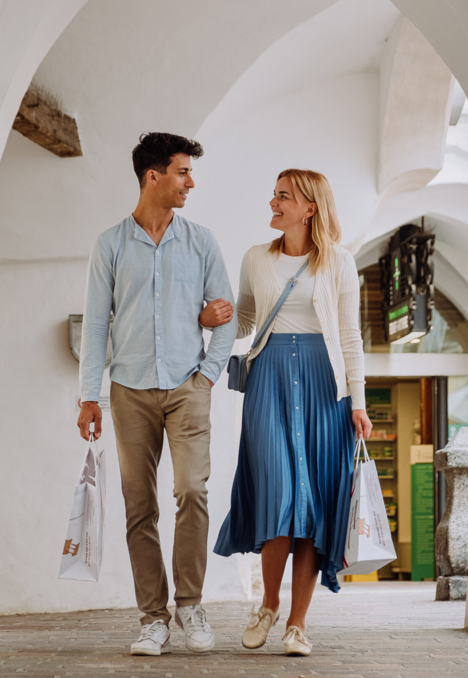 Couple walking through an arched white passage in Brixen Südtirol with shopping bags.