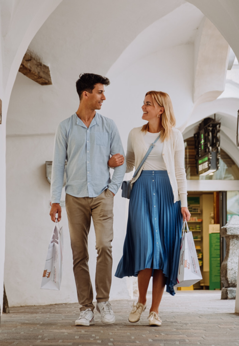 Coppia che passeggia sotto un passaggio ad archi bianco a Brixen Südtirol con borse per lo shopping.