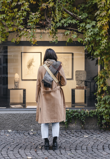 Person steht auf einem Kopfsteinpflasterweg und schaut in ein von Efeu umranktes Schaufenster.