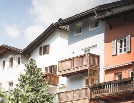 Colorful houses with wooden balconies and a tree in Brixen Südtirol under a partly cloudy sky.