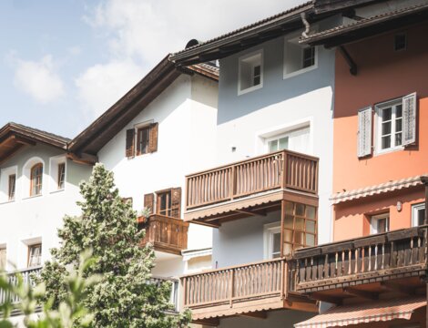 Bunte Häuser mit Holzbalkonen und einem Baum in Brixen Südtirol unter leicht bewölktem Himmel.