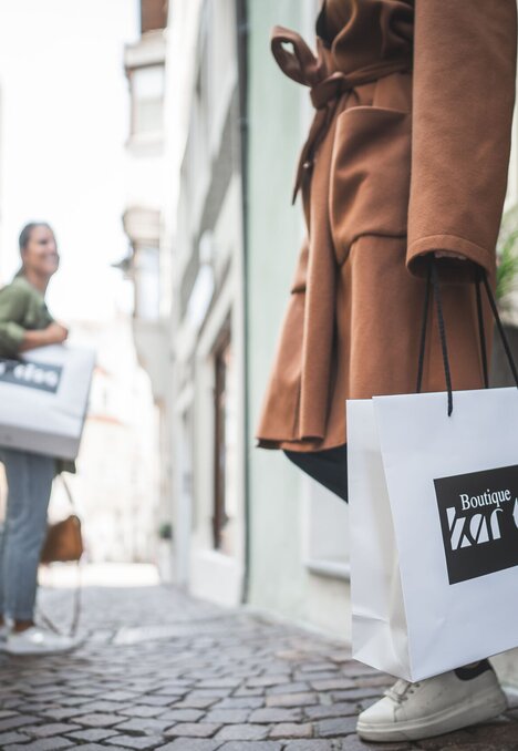 Eine Person trägt Einkaufstüten durch eine schmale Kopfsteinpflastergasse in Brixen Südtirol.