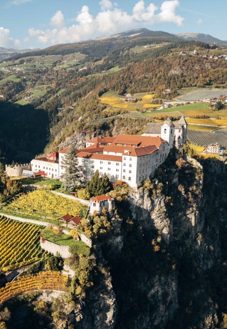 Historisches Kloster auf einem Felsen über Weinbergen in Brixen Südtirol, mit Bergen und Tal.